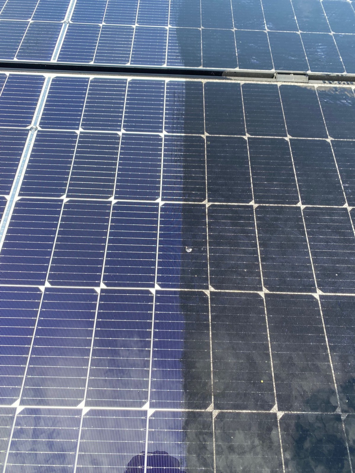 Panneau photovoltaïque nettoyé sur sa moitié gauche, d'un bleu franc, et encore couvert d'un film gris sur sa moitié droite