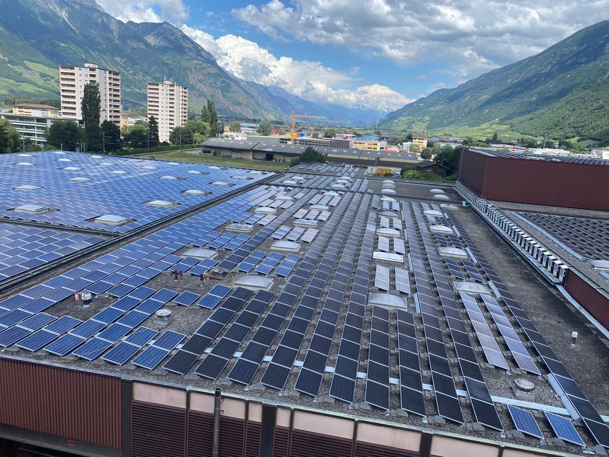 Bâtiment industriel avec toiture photovoltaïque, chaîne de montagnes en arrière-plan