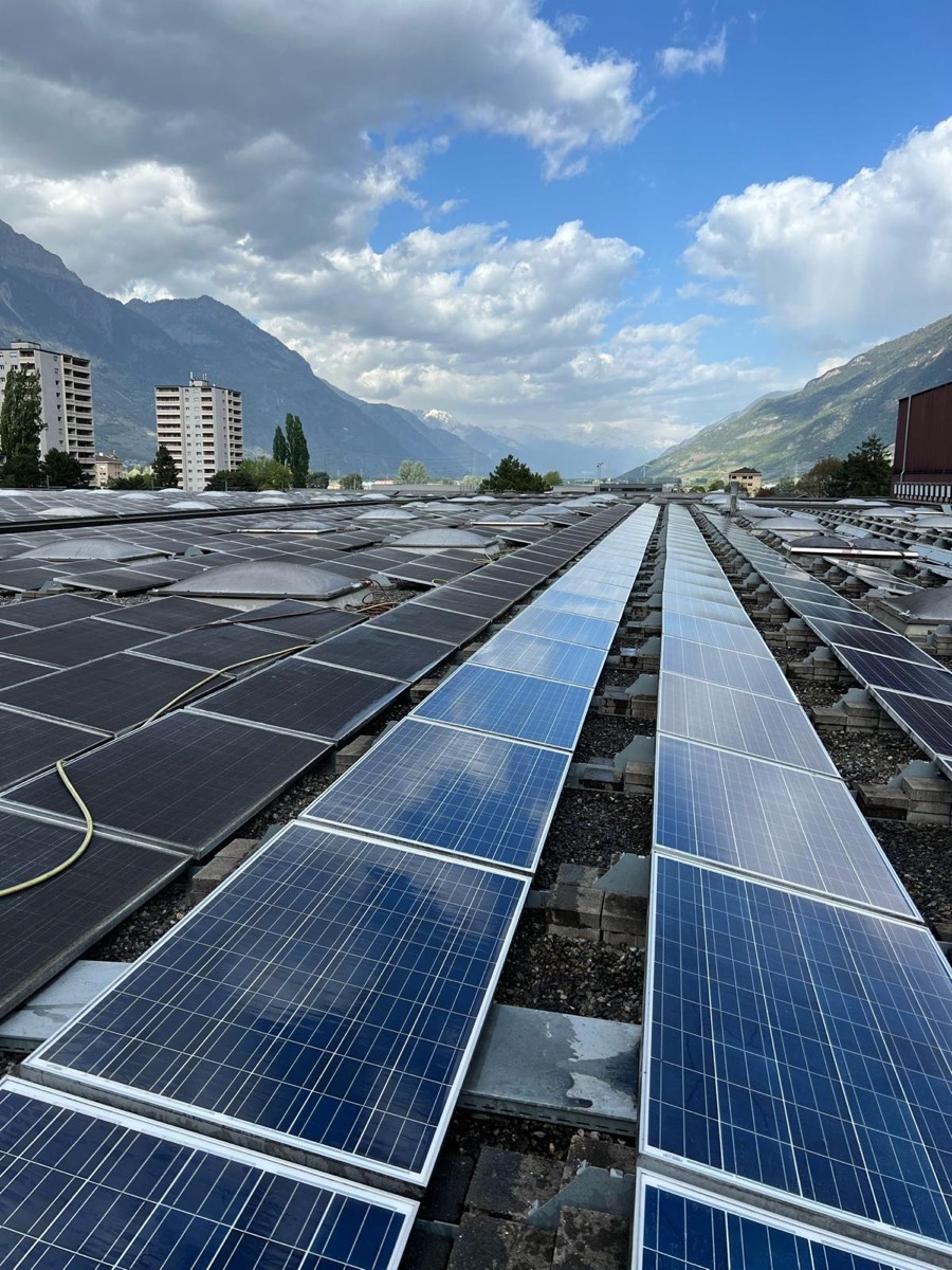 Grande toiture industrielle en Valais couverte de rangées de panneaux, montagnes en arrière-plan