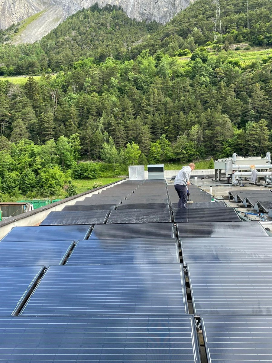 Toiture couverte de panneaux photovoltaïques en lisière de forêt, un technicien au fond