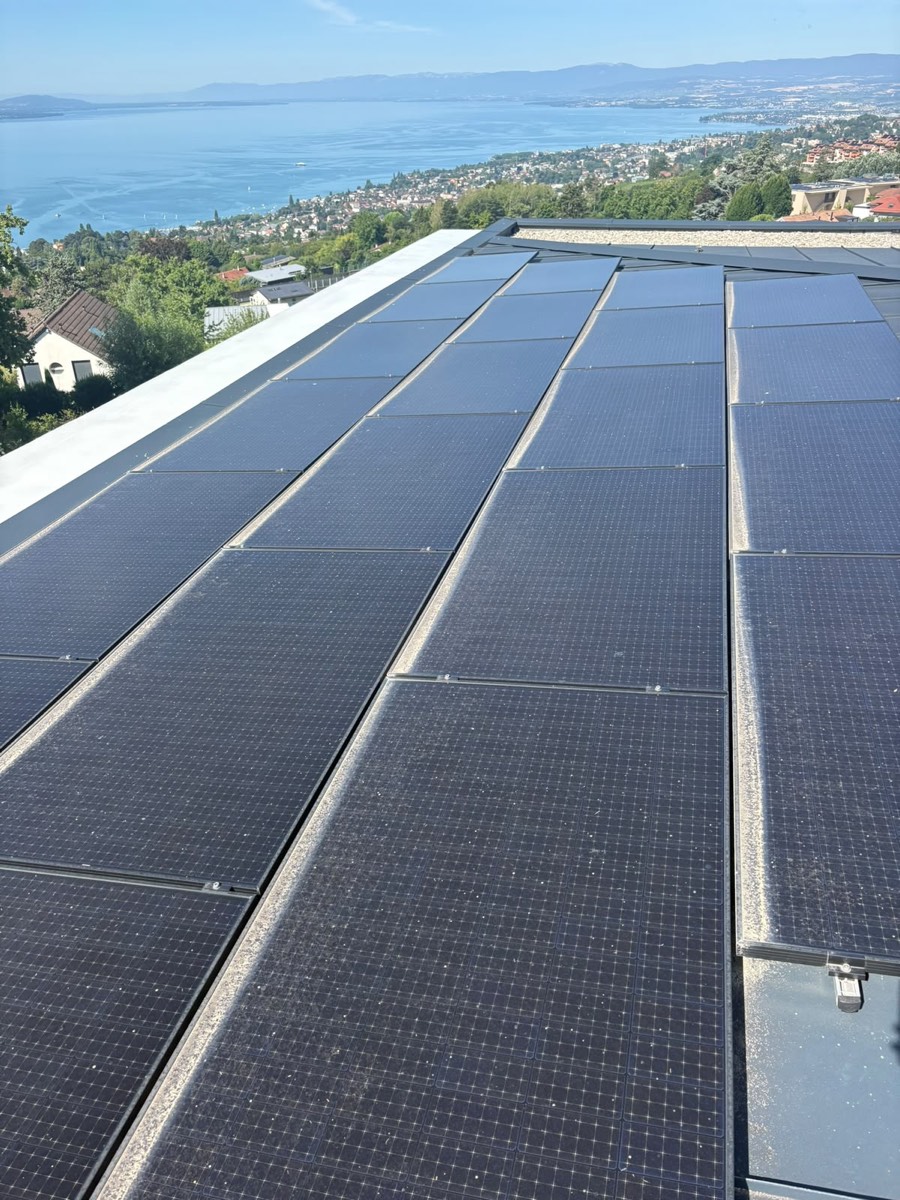 Panneaux photovoltaïques posés sur une toiture-terrasse, jardin et village en arrière-plan