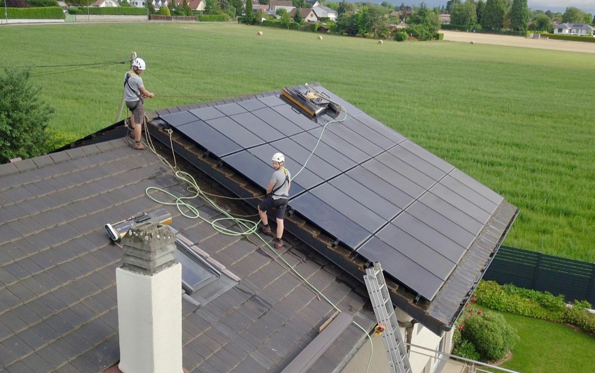 Vue aérienne d'une villa dont la toiture photovoltaïque est nettoyée par deux techniciens casqués