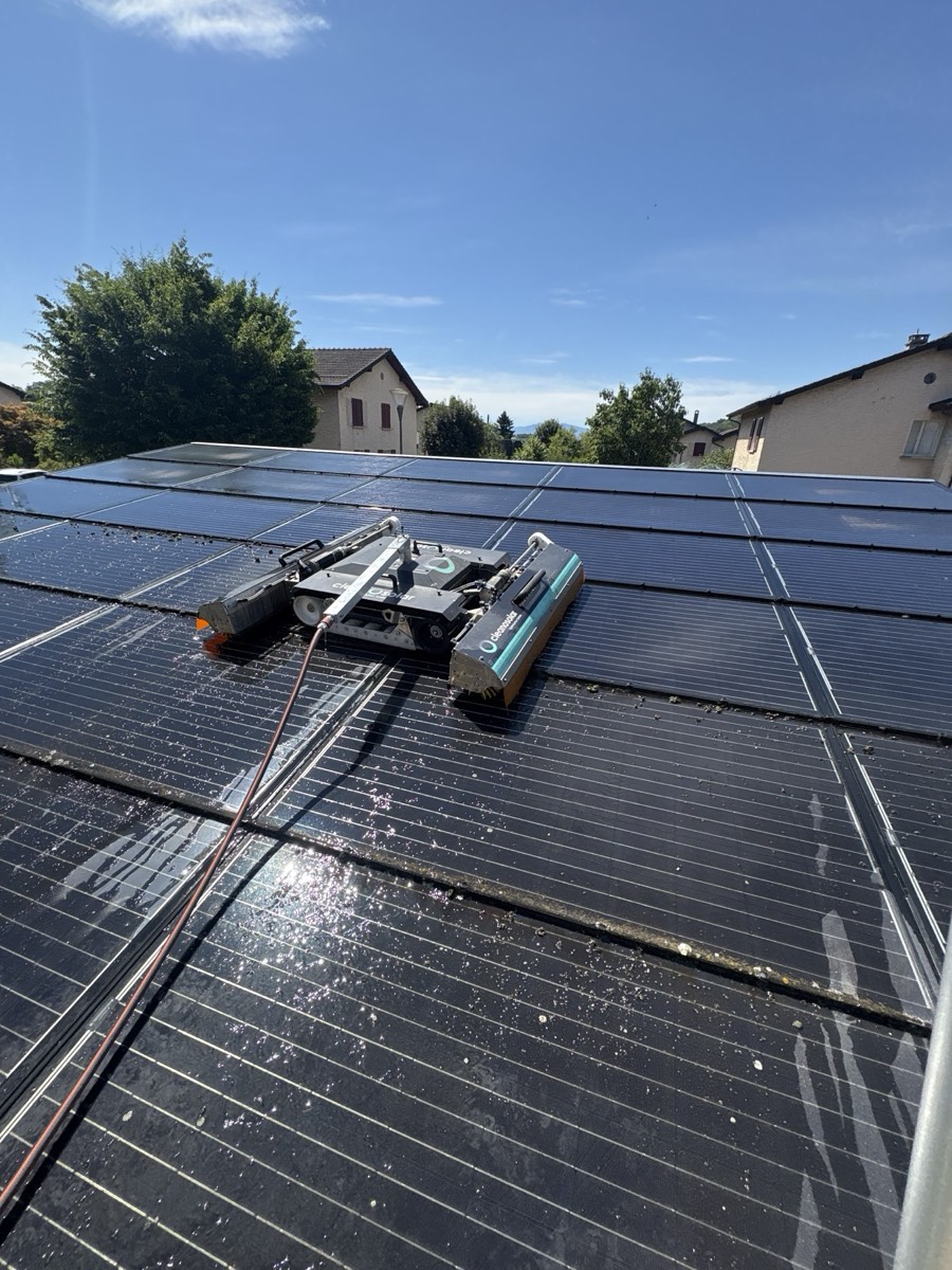 Robot Cleanosolar sur une toiture résidentielle sombre, traces de nettoyage visibles derrière lui