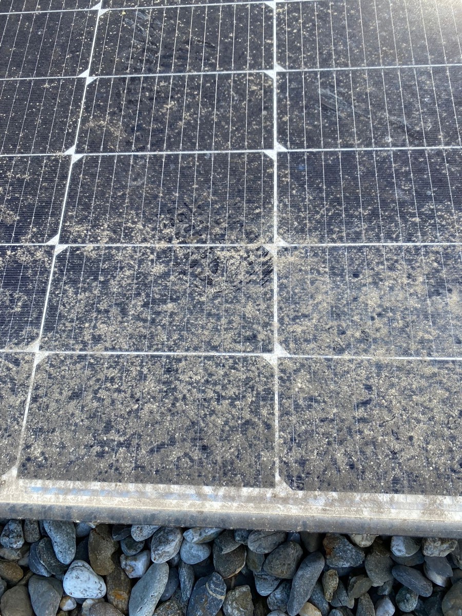 Panneaux photovoltaïques d'une toiture plate industrielle couverts d'une croûte beige sèche, lit de gravier au premier plan